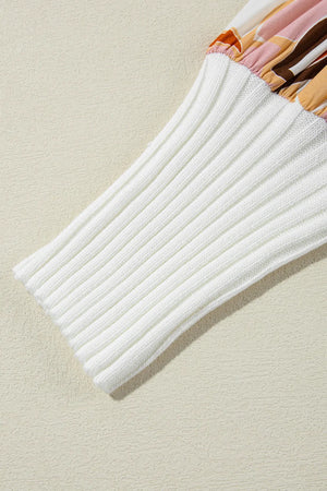 White ribbed knit sweater sleeve with a colorful abstract floral print fabric detail at the cuff.