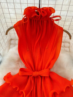Orange pleated midi dress with ruffled neckline and belted waist.