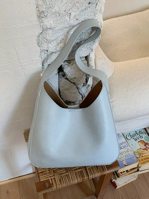 Sleek light blue PU leather shoulder bag with curved strap and open top.