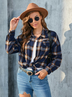 Plaid button-up shirt in dark blue with tan and white plaid, featuring chest pockets and a knotted hem.