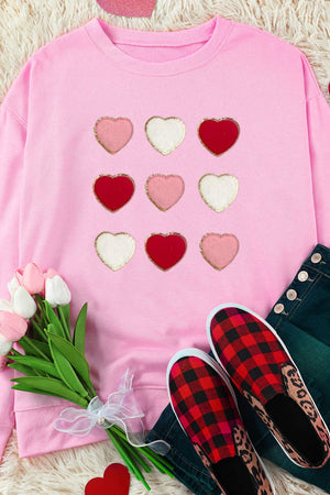Blush pink sweatshirt with a grid of embellished hearts in red, pink, and white.