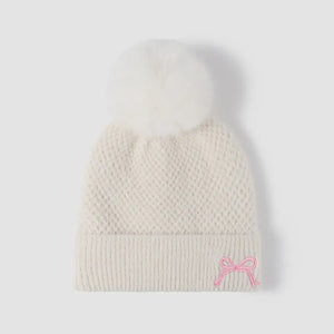 White textured knit beanie with white pom-pom and pink bow detail