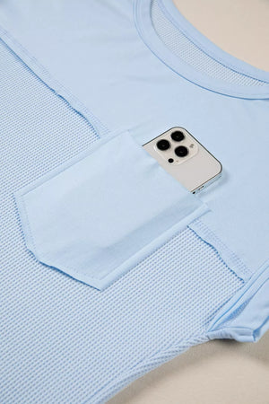 Light blue waffle knit t-shirt with pocket holding a phone and curved hem detail.
