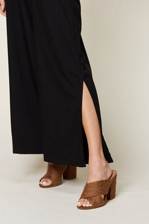 Black jumpsuit with high slit legs, styled with brown woven heeled mules.