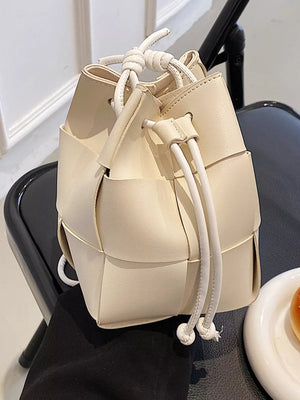 Chic woven mini bucket bag in white with drawstring closure and knotted handles.