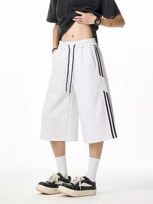 Grey sweatpants with drawstring and black side stripes, cropped length.