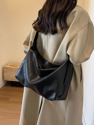 Black leather shoulder bag with adjustable strap, worn by a woman.