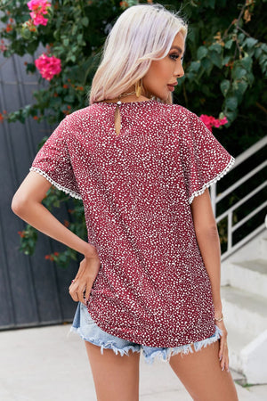 Burgundy dotted blouse with flutter sleeves and pom-pom trim.
