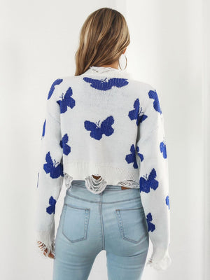 White cropped knit sweater with distressed details and a blue butterfly print.