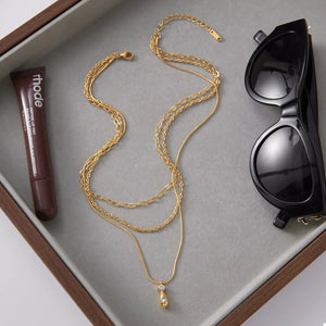 Gold three layered pendant necklace with a teardrop charm and two small crystals.