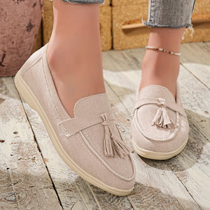 Beige faux-suede slip-on loafers with decorative tassels and contrast stitching.