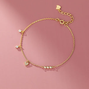 Gold pavé heart charm bracelet with cubic zirconia accents and three small heart charms.