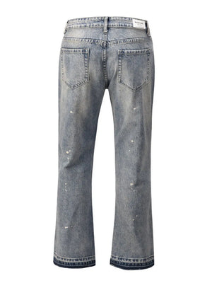 Distressed wash bootcut jeans with raw hem and paint splatters.