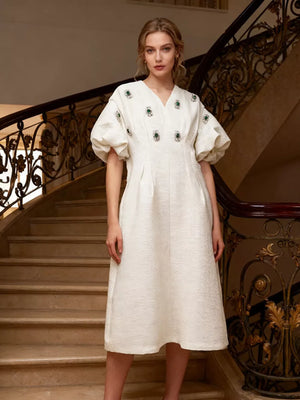 White midi dress with puff sleeves, V-neck, and rhinestone embellishments.