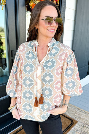 Geometric print blouse with tassel tie, featuring a ruffled neckline and balloon sleeves.