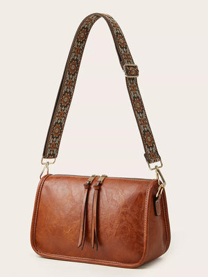 Tan leather crossbody bag with a patterned strap and tassel zipper pulls.