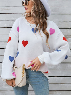 White knit sweater with bubble sleeves and a scattered heart motif in pink, red, and blue.