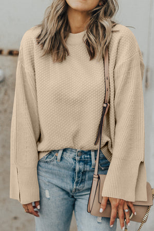 Beige textured knit sweater with crewneck and split sleeves, styled with jeans.
