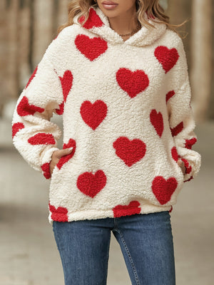 Cream sherpa hoodie with all-over red heart print and front pockets.