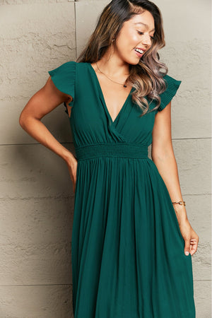 Emerald green pleated flutter sleeve maxi dress with smocked waist and V-neck.