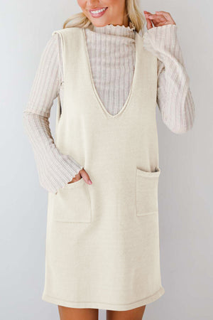 Cream sleeveless knit V-neck dress with two front pockets, layered over a ribbed turtleneck.