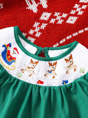 Green A-line baby dress with smocked white yoke featuring embroidered Santa, reindeer, and trees.