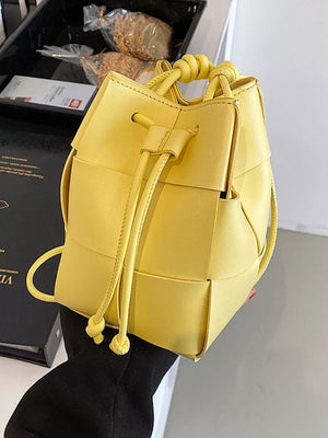 Yellow woven mini bucket bag with drawstring and knotted top handle.