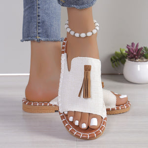 White open-toe slide sandals with brown tassel detail and decorative stitching.