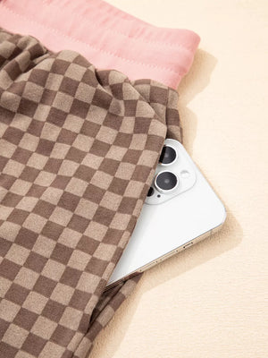 Chic checkerboard loungewear shorts in brown with a pink waistband, showing a phone pocket detail.