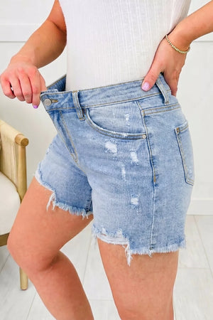 Light wash denim shorts with whiskering, distressed details, and a raw hem.