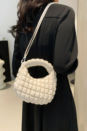 Padded crescent crossbody bag in ivory with sculptural texture and white strap.