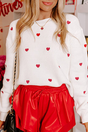 White ribbed crewneck sweater with all-over red heart embroidery.