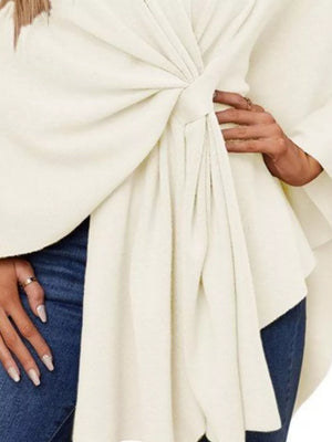 Eggshell knit cape top with tie-front detail and draped elegance.