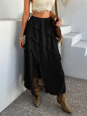 Black midi skirt with cascading ruffles and a high slit, styled with boots.