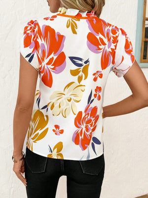 Frilled tie-neck maternity blouse with a vibrant floral print and short sleeves.