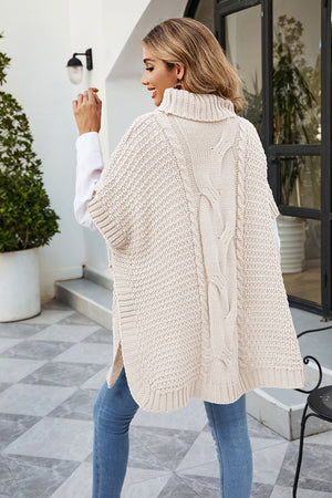 Cream cable knit turtleneck poncho with side slits and a split back detail.