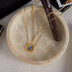 Gold-plated layered necklace with blue stone pendant and delicate chains.