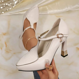 Elegant white pointed toe T-strap pumps with gold buckle and charm detail.