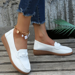 White leather loafers with braided detail and a brown sole.