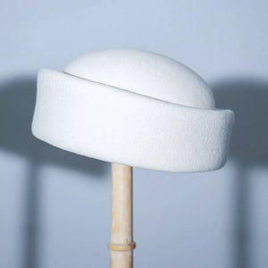 White wool pillbox hat with a curved brim, displayed on a stand.