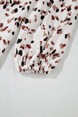 High-neck abstract print blouse in white with black and brown spots, featuring a gathered elastic cuff.