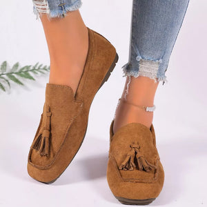 Brown suede slip-on loafers with tassel embellishments and a square toe.