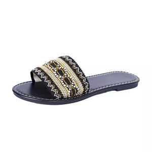 Black open-toe slide sandals with intricate gold and white bead embroidery on the strap.