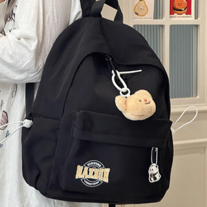 Black nylon backpack with plush bear and panda charms, front pocket with logo patch.