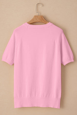 Pink knit top with short sleeves and crew neck, featuring daisy appliqué detail.