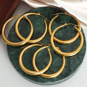 Sculpted oval gold hoop earrings, 18K gold-plated, displayed on a green marble surface.