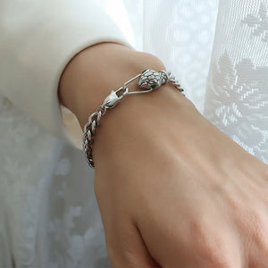 Serpentine chain bracelet in silver with green jeweled snake head detail.
