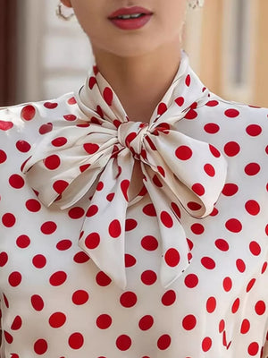 White polka dot shirt with a large red bow tie neck and cap sleeves.