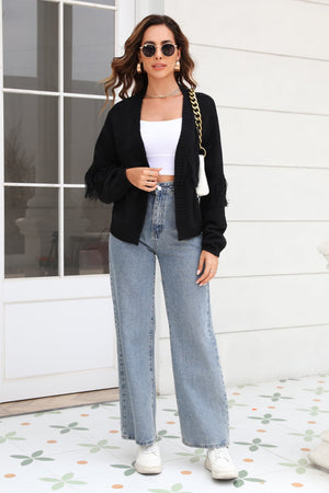 Black acrylic cardigan with fringe sleeves and open front, styled with a white crop top and jeans.