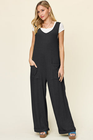 Black ribbed knit tie-strap jumpsuit with wide legs and front pockets.